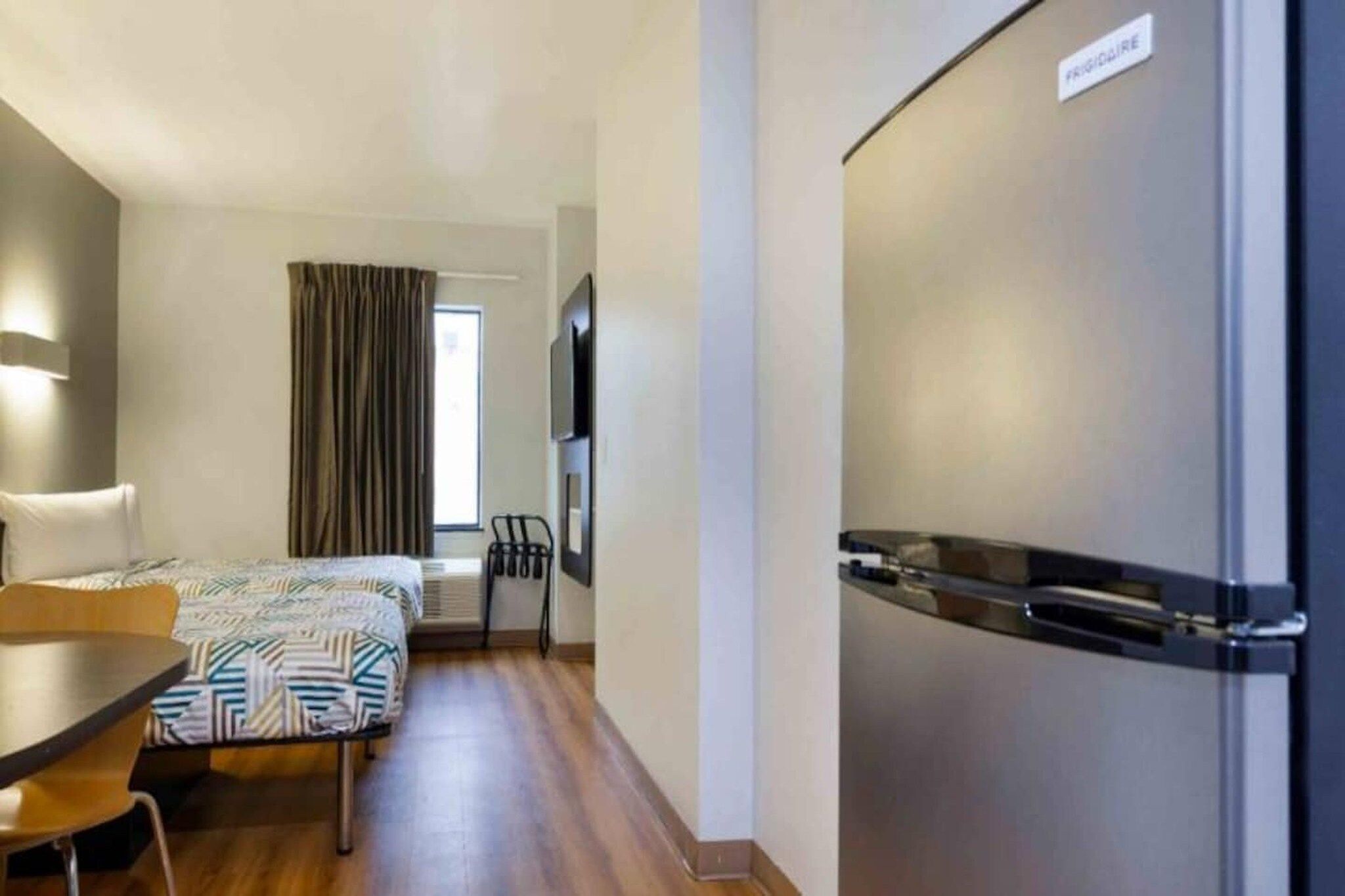 A hotel room with a bed, a desk, a chair, a television, and a refrigerator.
