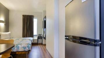 A hotel room with a bed, a desk, a chair, a television, and a refrigerator.