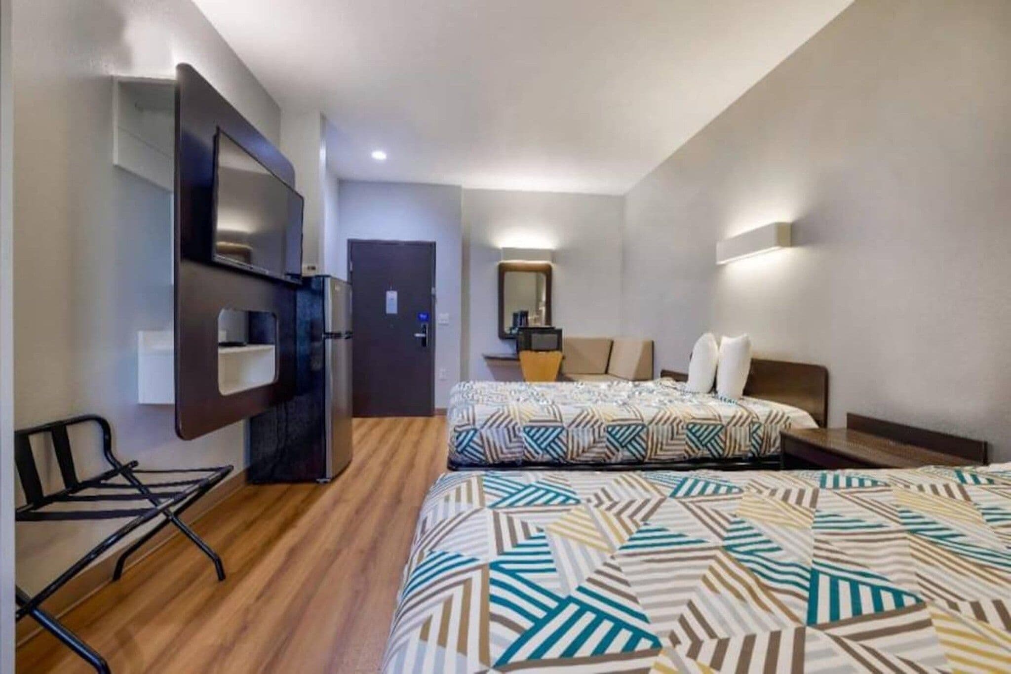 Une chambre d’hôtel avec deux lits, un bureau, une chaise, une télévision et un miroir.