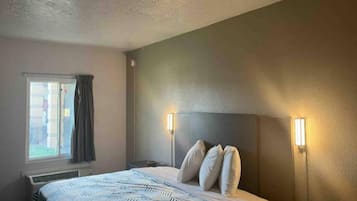 A hotel room with a bed, two bedside lamps, a window with curtains, and a thermostat.