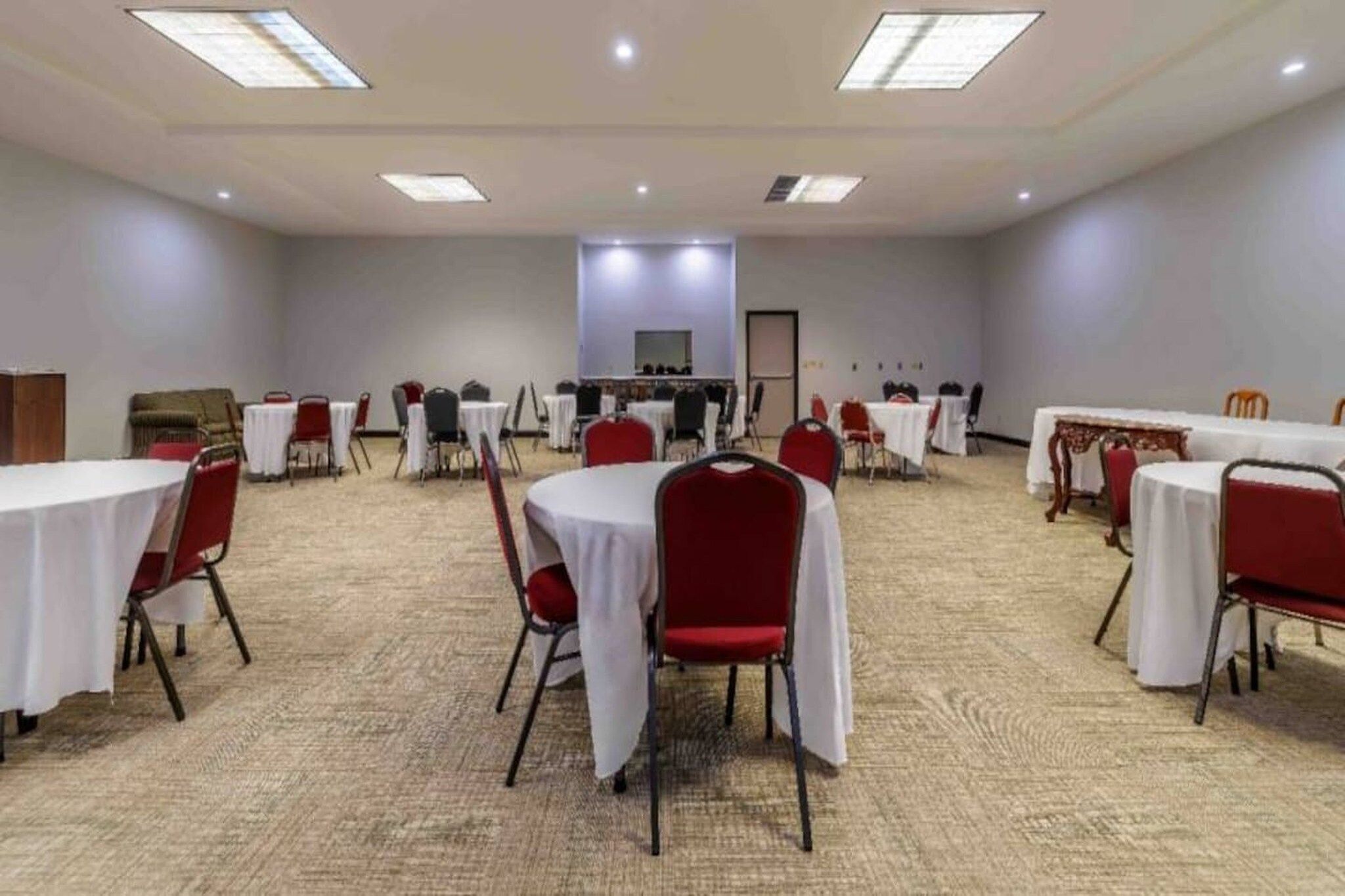 A conference room with round tables, red chairs, and carpeted flooring.