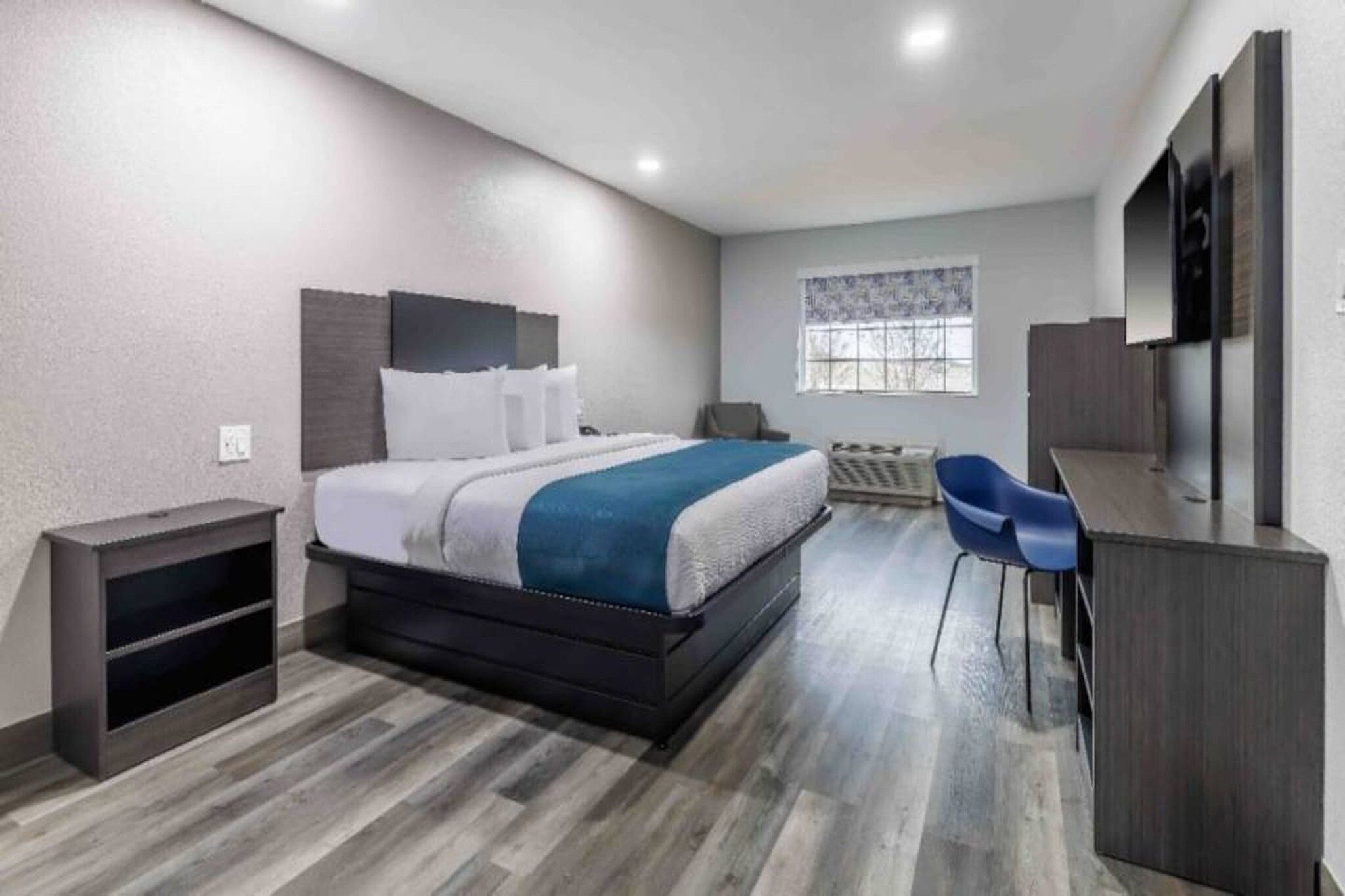 A modern bedroom with a bed, a desk, a chair, and a window.
