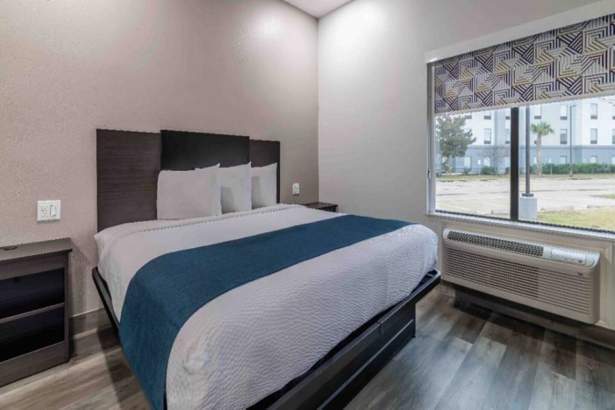Une chambre d’hôtel avec un lit, une table de chevet, une fenêtre donnant sur un paysage agréable et un climatiseur fixé au mur.