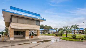 A hotel with a flat roof, a covered entrance, and a parking lot with a water feature.
