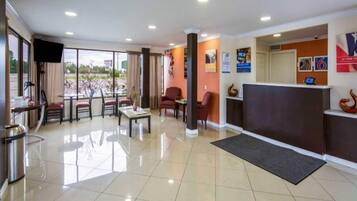 A hotel lobby with a reception desk, seating area, and a view of the outdoors.