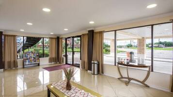 A hotel lobby with a reception desk, a coffee machine, and a large window offering a view of the parking area.