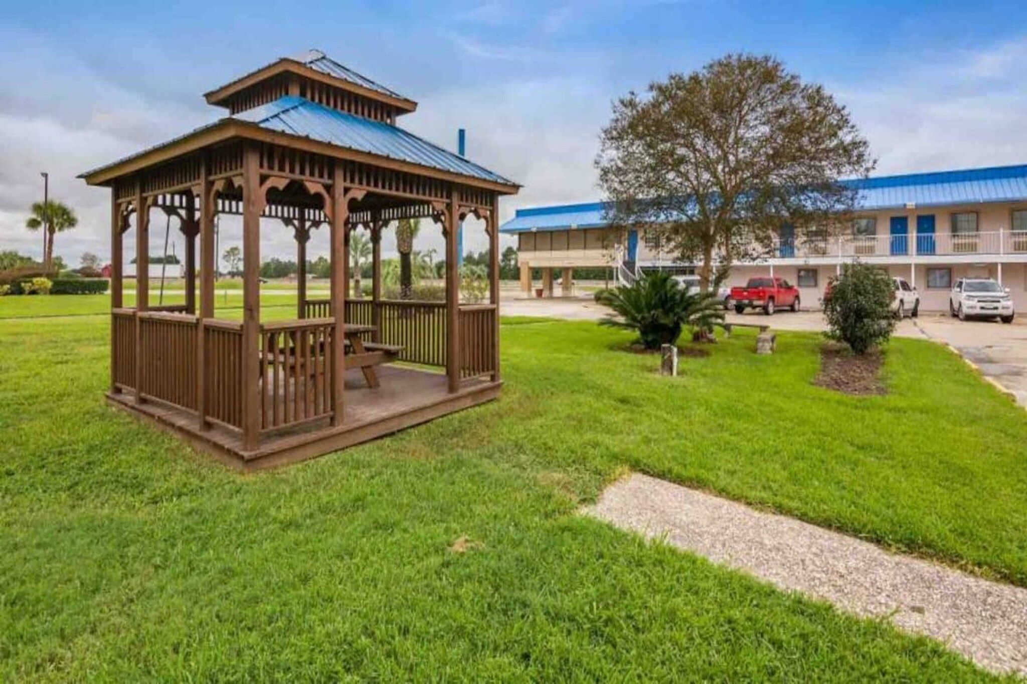 Un kiosque doté d’un toit et de côtés ouverts, un bâtiment avec un toit bleu et une aire de stationnement avec des voitures.
