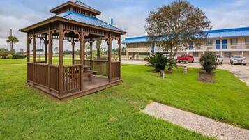 Un kiosque doté d’un toit et de côtés ouverts, un bâtiment avec un toit bleu et une aire de stationnement avec des voitures.