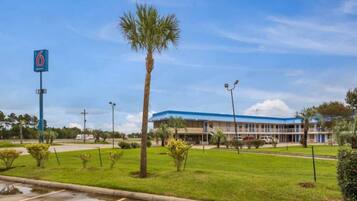 A hotel with a blue roof, a parking lot, and a palm tree.