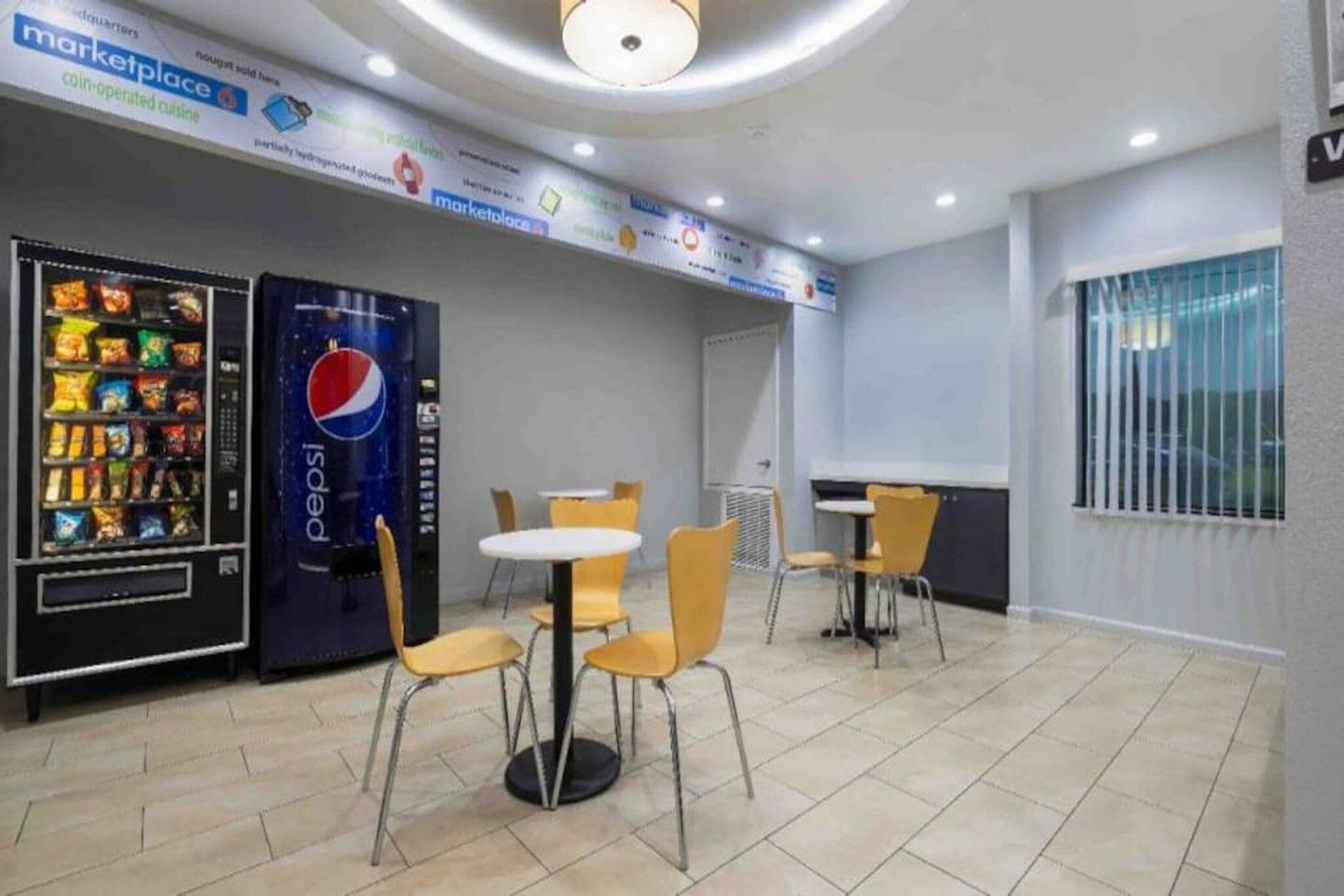 Une cafétéria équipée de distributeurs automatiques, de tables et de chaises.