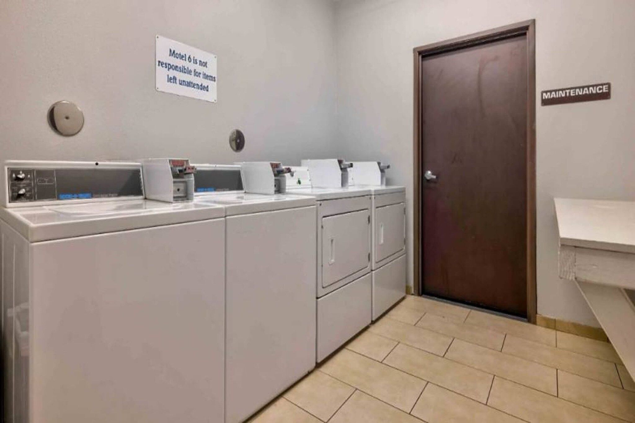 Une buanderie équipée de plusieurs machines à laver, un panneau indiquant que « le motel 6 n’est pas responsable des objets laissés sans surveillance » et une porte marquée « ENTRETIEN ».