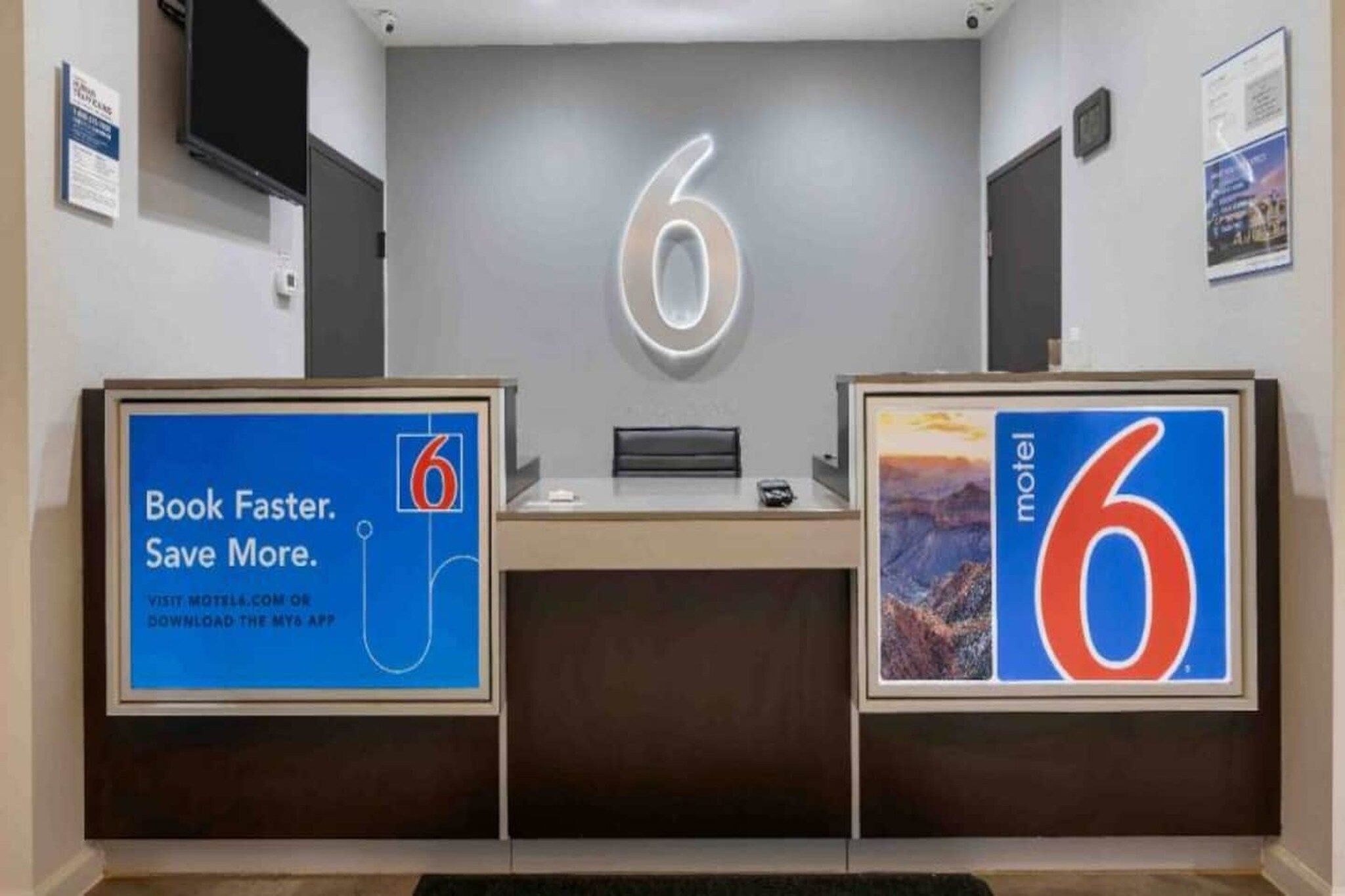 A reception desk with a large illuminated number 6 on the wall, two framed signs advertising the number 6, and a counter with a computer.