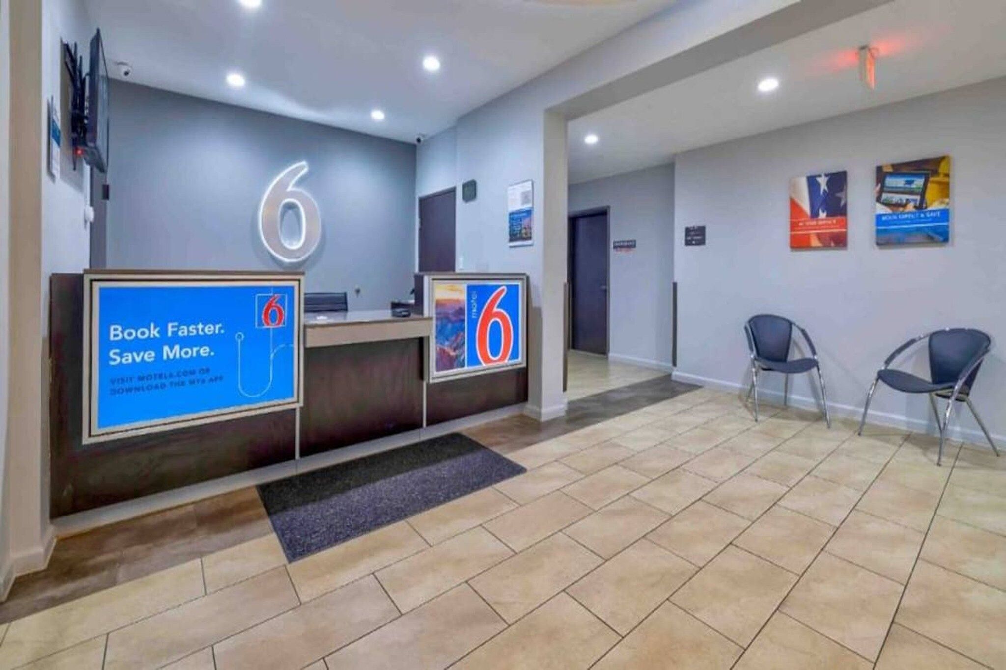 A hotel reception area with two reception desks, a tiled floor, and a few chairs.