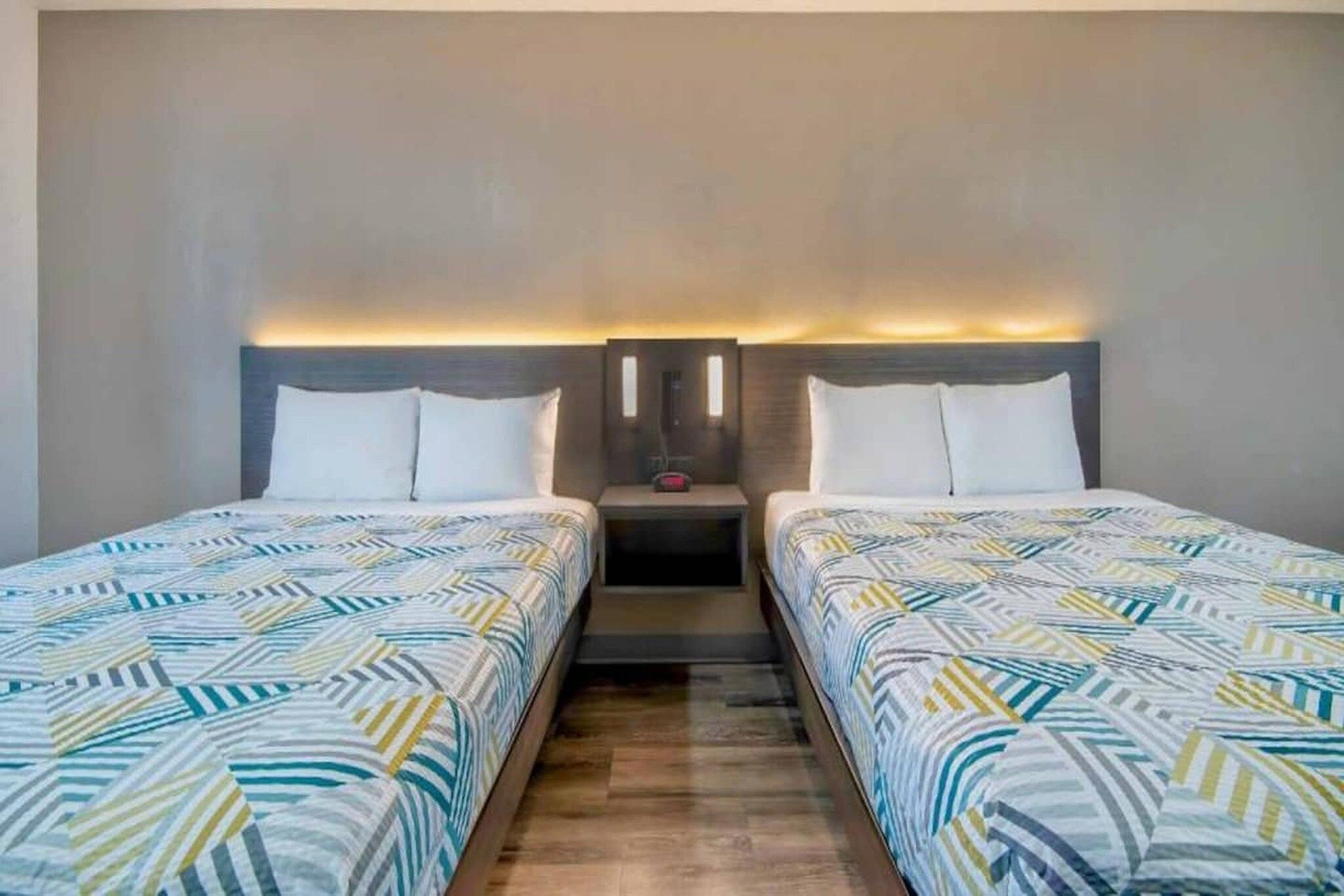 Habitació d'hotel amb dos llits, una tauleta de nit i una làmpada de paret.