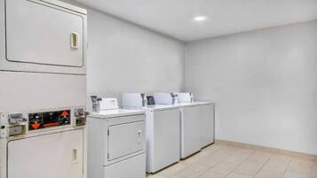 A laundry facility with stacked washing machines and dryers, a control panel, and a tiled floor.