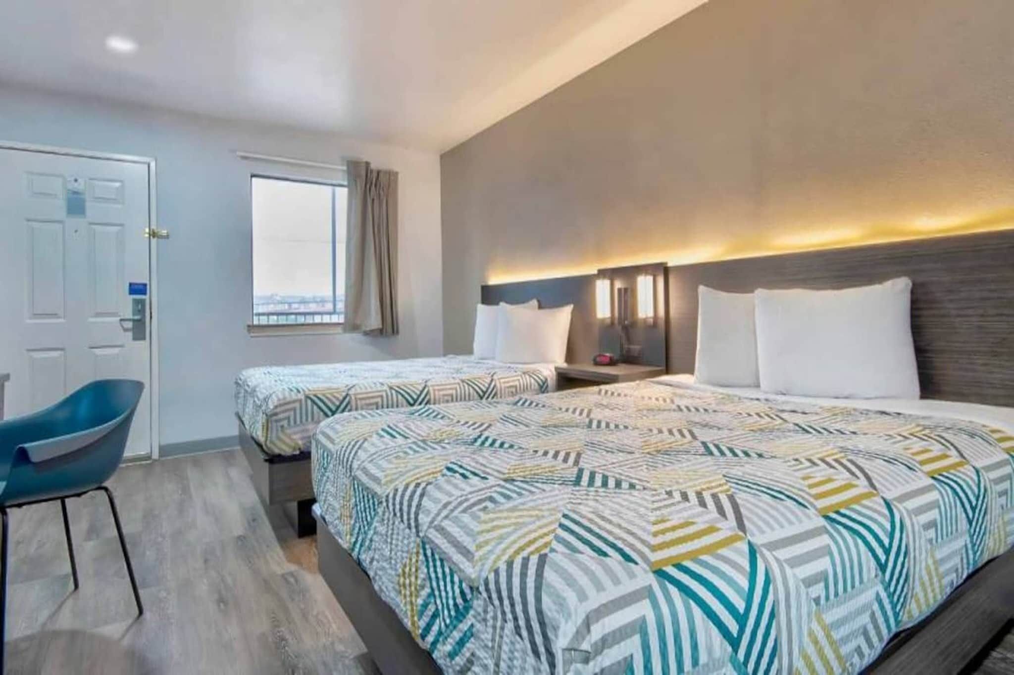 A hotel room with two beds, a desk, a chair, and a window with curtains.