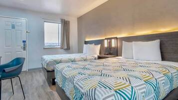A hotel room with two beds, a desk, a chair, and a window with curtains.