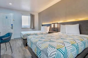 Une chambre d’hôtel avec deux lits, un bureau, une chaise et une fenêtre avec des rideaux.