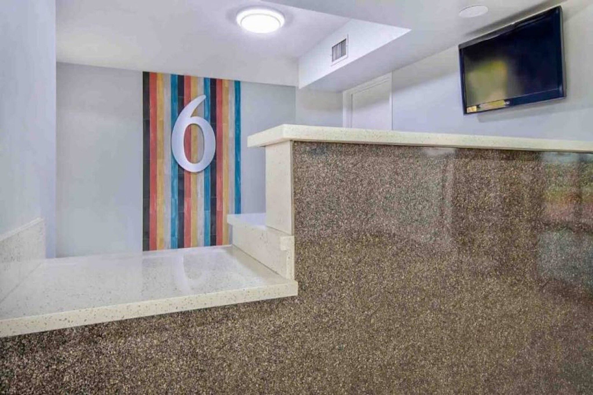 A reception area with a large number '6' on the wall, a flat-screen TV mounted on the wall, and a granite counter.
