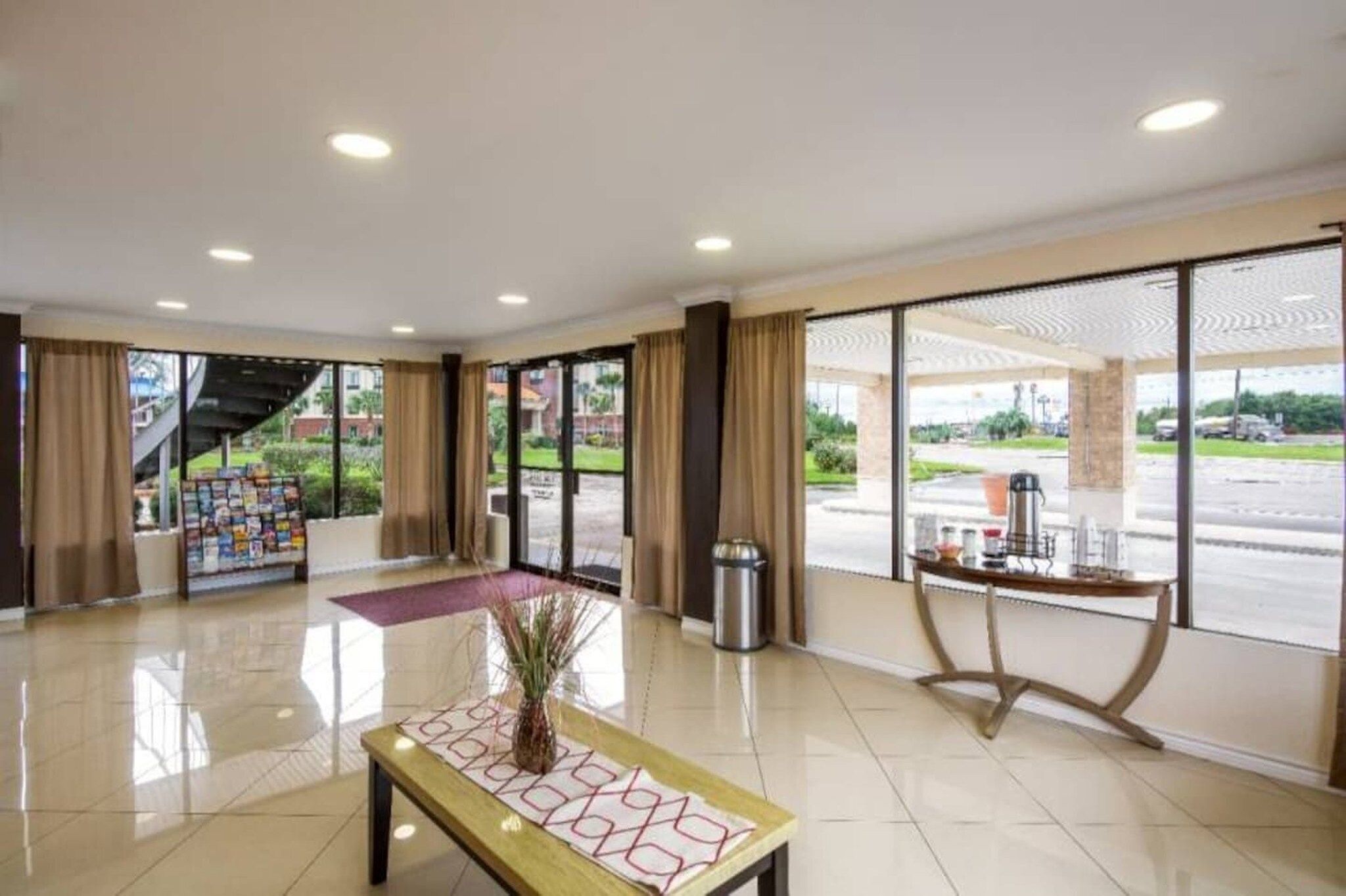 A hotel lobby with a reception desk, a coffee machine, and a large window offering a view of the parking area.