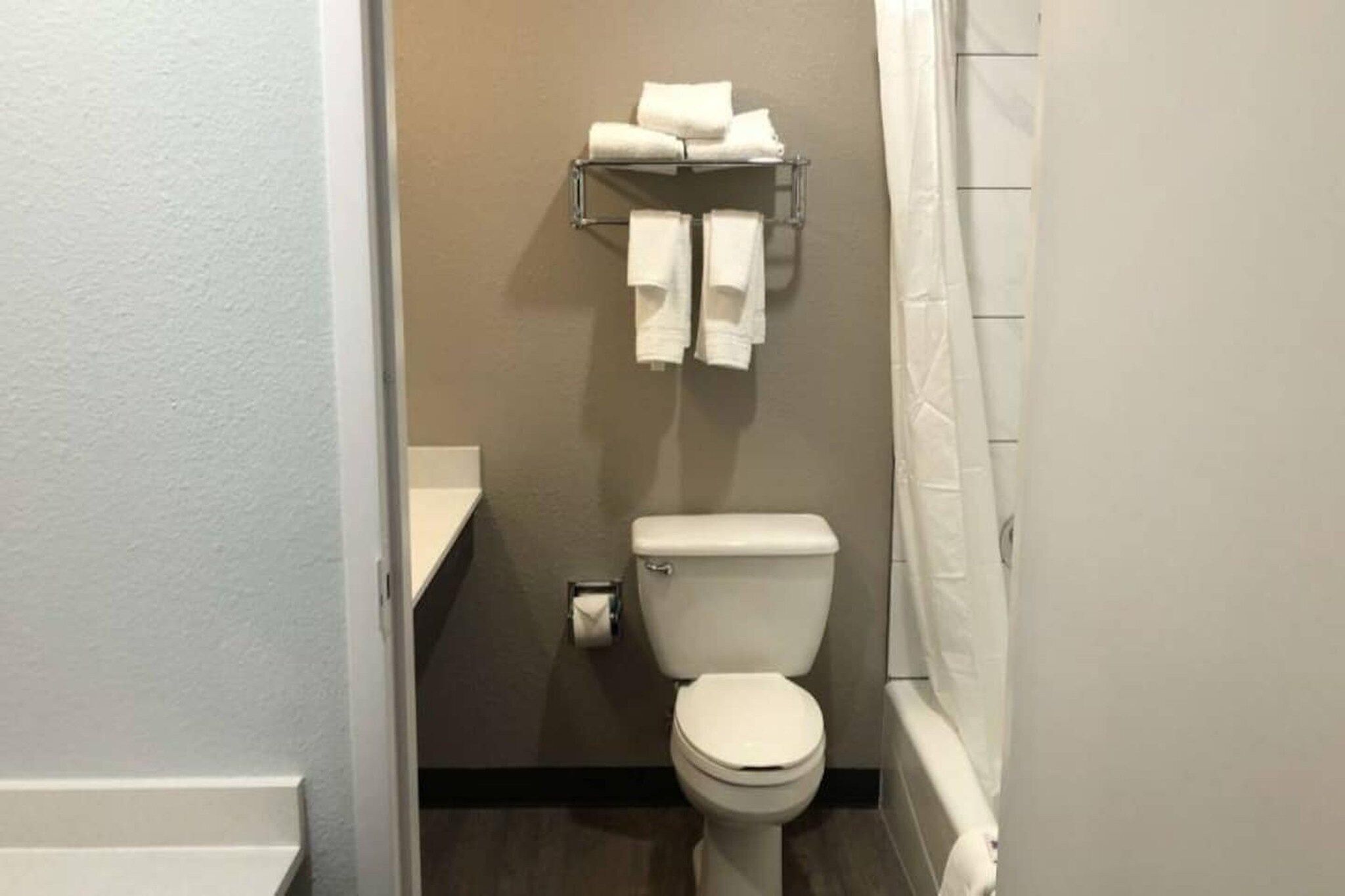 A small, clean bathroom with a toilet, a towel rack with folded towels, and a shower curtain.