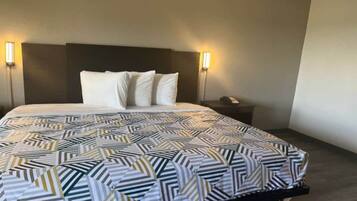 A hotel room with a bed, two bedside lamps, a nightstand, and a patterned bedspread.