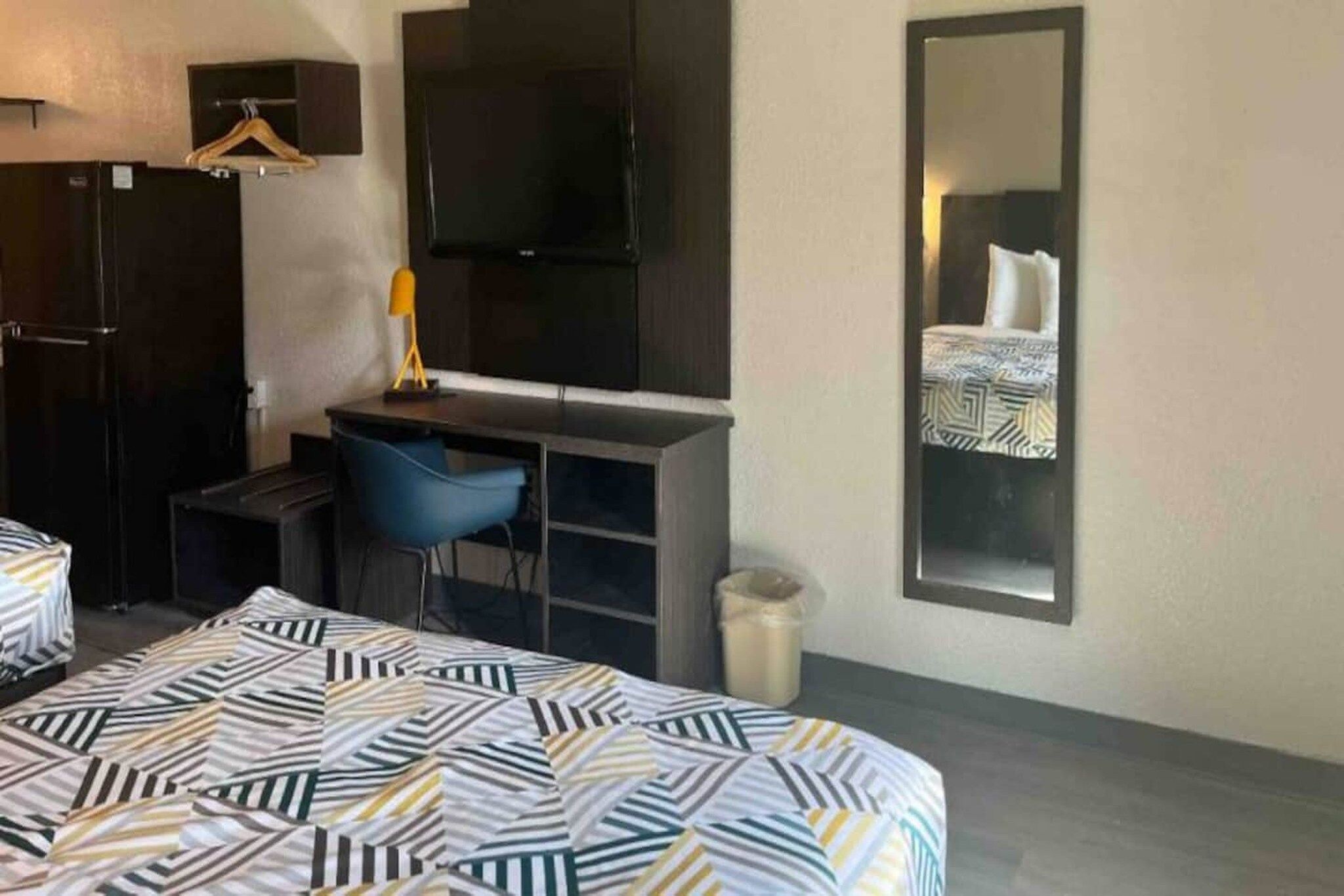 A hotel room with a bed, a desk, a chair, a TV, a mirror, and a wardrobe.