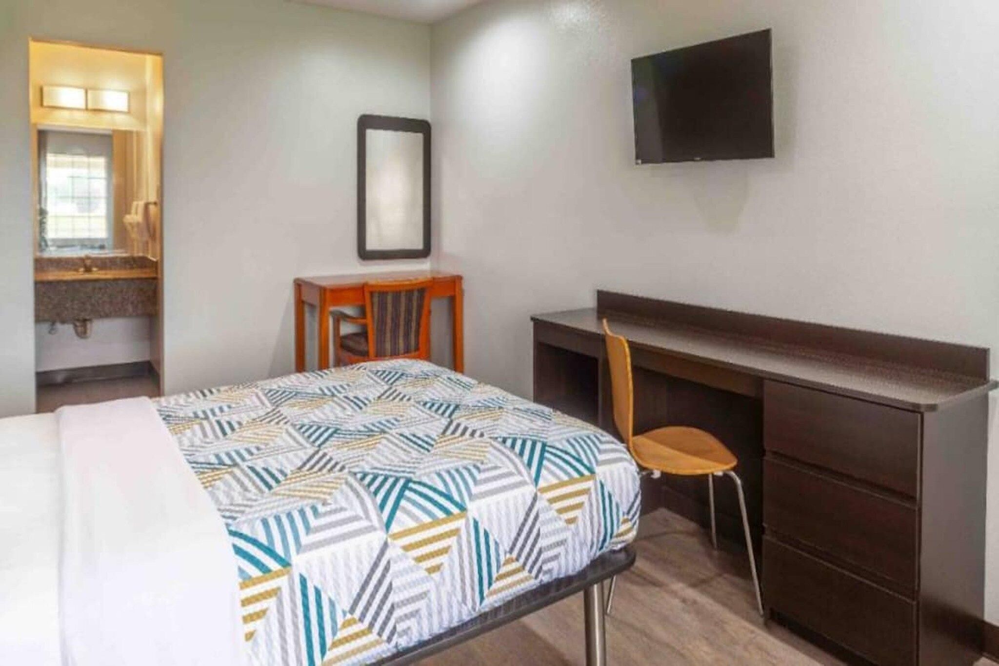 Une chambre d’hôtel équipée d’un lit, d’un bureau, d’une chaise, d’un téléviseur à écran plat et d’un miroir.