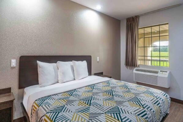 A hotel room with a bed, a window with curtains, and an air conditioning unit.