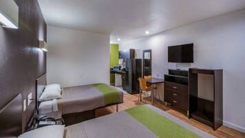 Een compacte hotelkamer met twee enkele bedden, een klein bureau, een stoel, een televisie en een kitchenette.