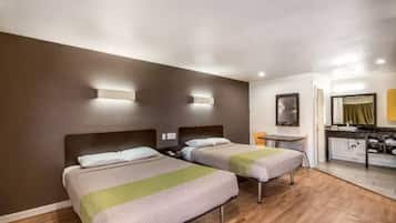 Una habitación de hotel con dos camas, una kitchenette pequeña y un baño con espejo y lavabo.