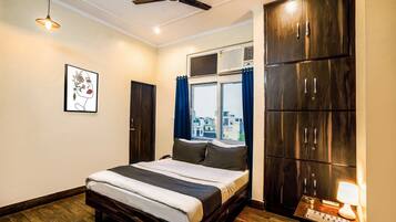 Une chambre à coucher comprenant un lit, un ventilateur de plafond, une fenêtre avec des rideaux, une armoire et une table de chevet avec une lampe.