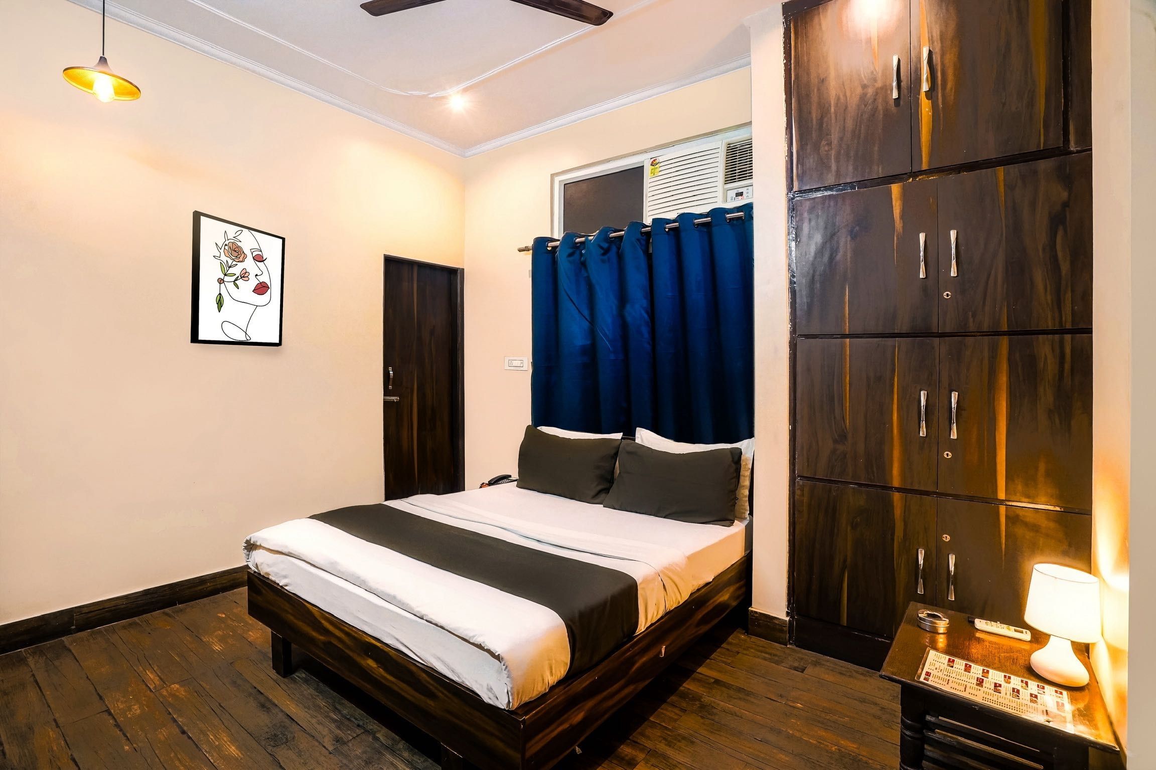 Une chambre à coucher comprenant un lit, une armoire, un ventilateur de plafond, un climatiseur fixé au mur et une œuvre d’art encadrée.