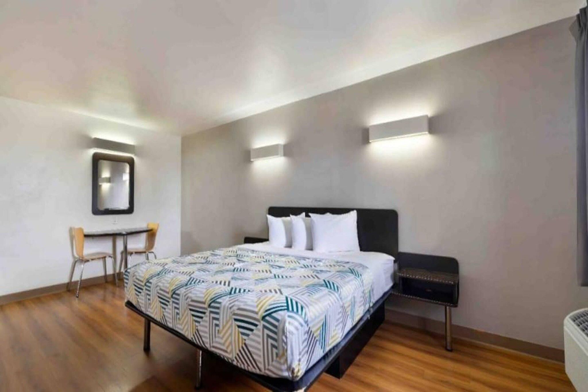 Een hotelkamer met een bed, nachtkastje, stoel en bureau met stoel.