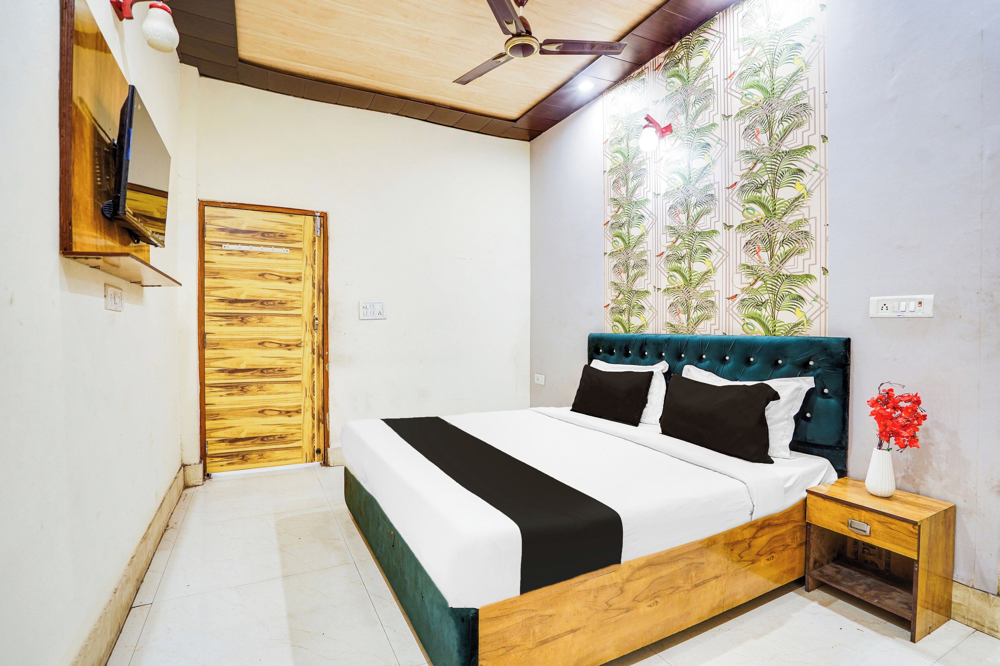A bedroom with a wooden bed frame, a ceiling fan, a wall-mounted TV, and a window with a geometric pattern.