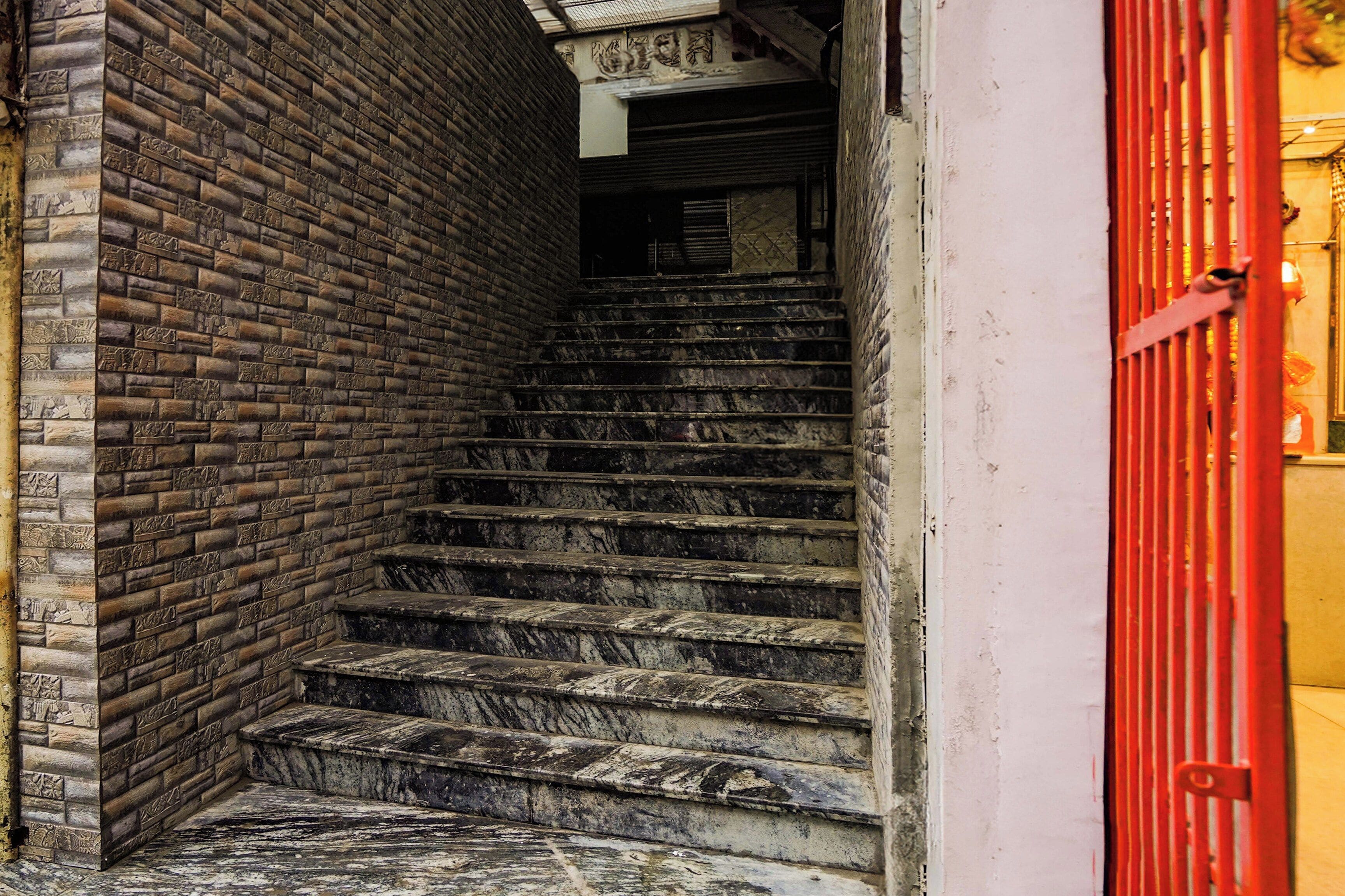 Un escalier, avec un mur de briques d’un côté et une porte rouge de l’autre.