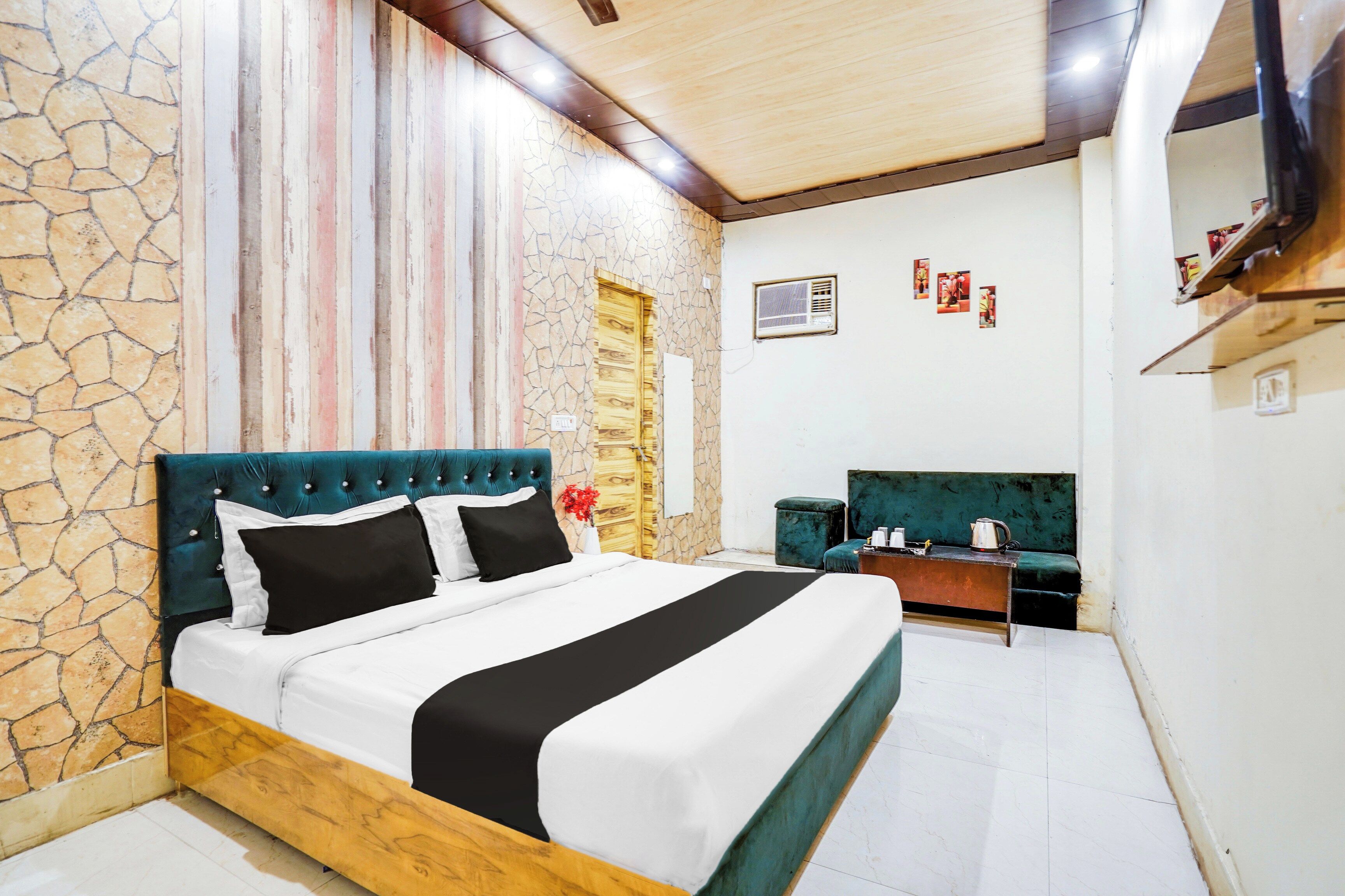 A hotel room with a stone wall, a bed with a wooden headboard, a small desk, and a green upholstered chair.
