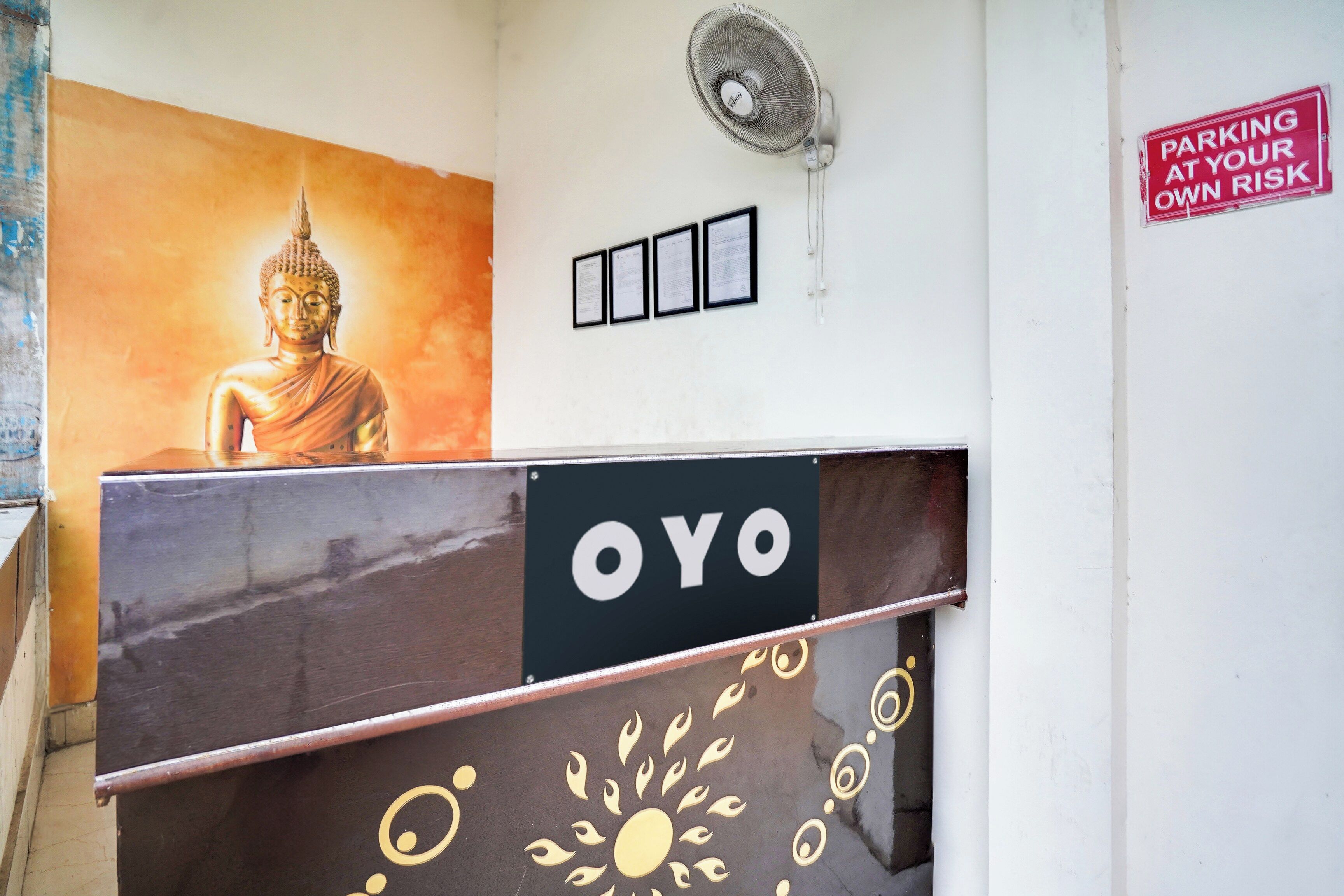 Un comptoir d’accueil orné d’une statue de Bouddha, d’un ventilateur et d’un panneau indiquant : « LE STATIONNEMENT SE FAIT SOUS VOTRE PROPRE RESPONSABILITÉ ».