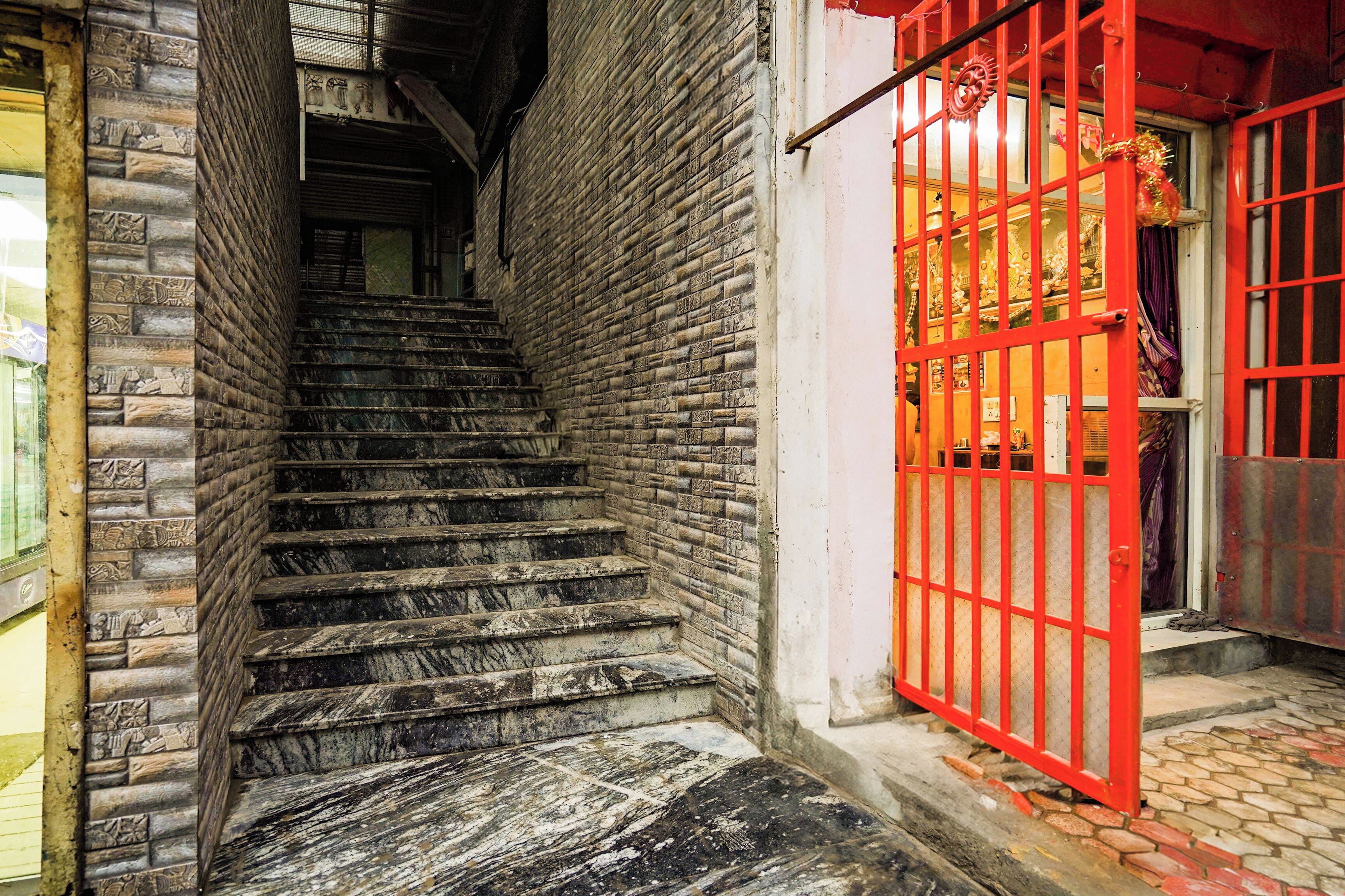A staircase leading to a red-walled room with a window displaying religious figures.