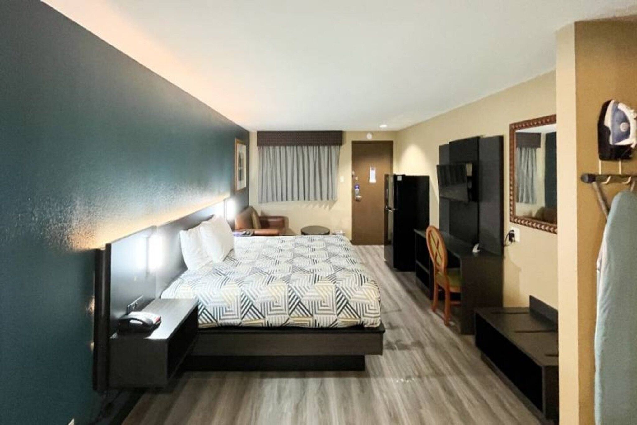A hotel room with a bed, a chair, a desk, a television, and a mirror.