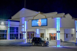 Ein Motel mit einem großen Schild mit der Zahl 6, einem Parkplatz und einem geparkten Fahrzeug davor.