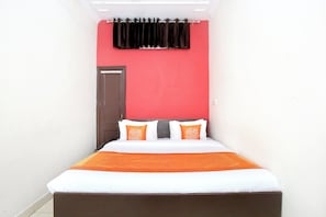 Una habitación de hotel estrecha con una cama, dos almohadas, una pared roja y una cortina negra.