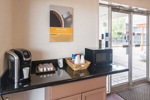 Ein Empfangsbereich mit Kaffeeautomat, Mikrowelle, einem Gebäckkorb und einer Kaffeetasse auf der Theke.