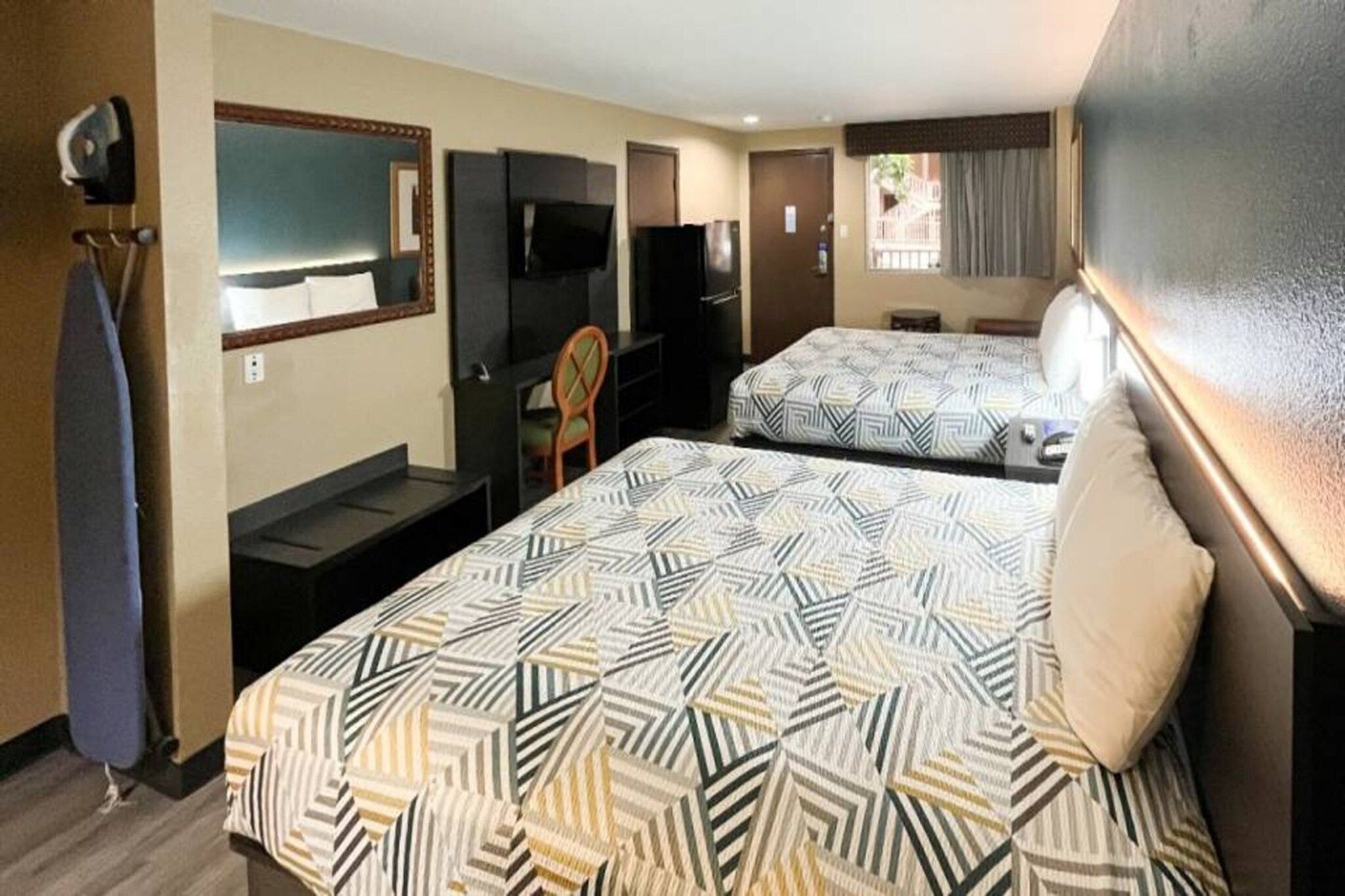 A hotel room with two beds, a desk, a chair, a television, and a mirror.