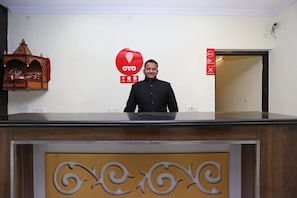 A man standing behind a reception desk with a red OYO logo and a no-smoking sign on the wall. - Hotel O Lime Wood (Dehradun)