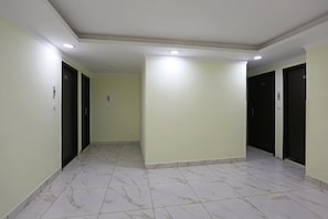 A corridor with a tiled floor, recessed ceiling lights, and doors on both sides. - Hotel O Lime Wood (Dehradun)