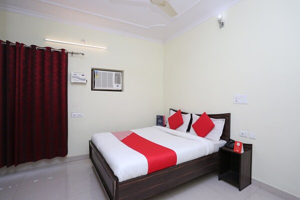 A hotel room with a bed, a nightstand, a red and white bedspread, a red curtain, and a ceiling fan. - Hotel O Lime Wood (Dehradun)
