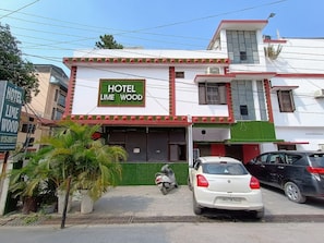 A hotel named 'Lime Wood' with a signboard, a parked white car, and a motorcycle in front. - Hotel O Lime Wood (Dehradun)