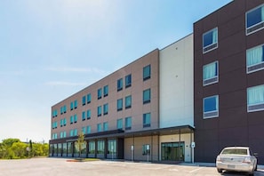 A modern hotel building with multiple floors, large windows, and a parking area with a car. - 1 Queen Bed | Micfridge | NSMK (Austin)