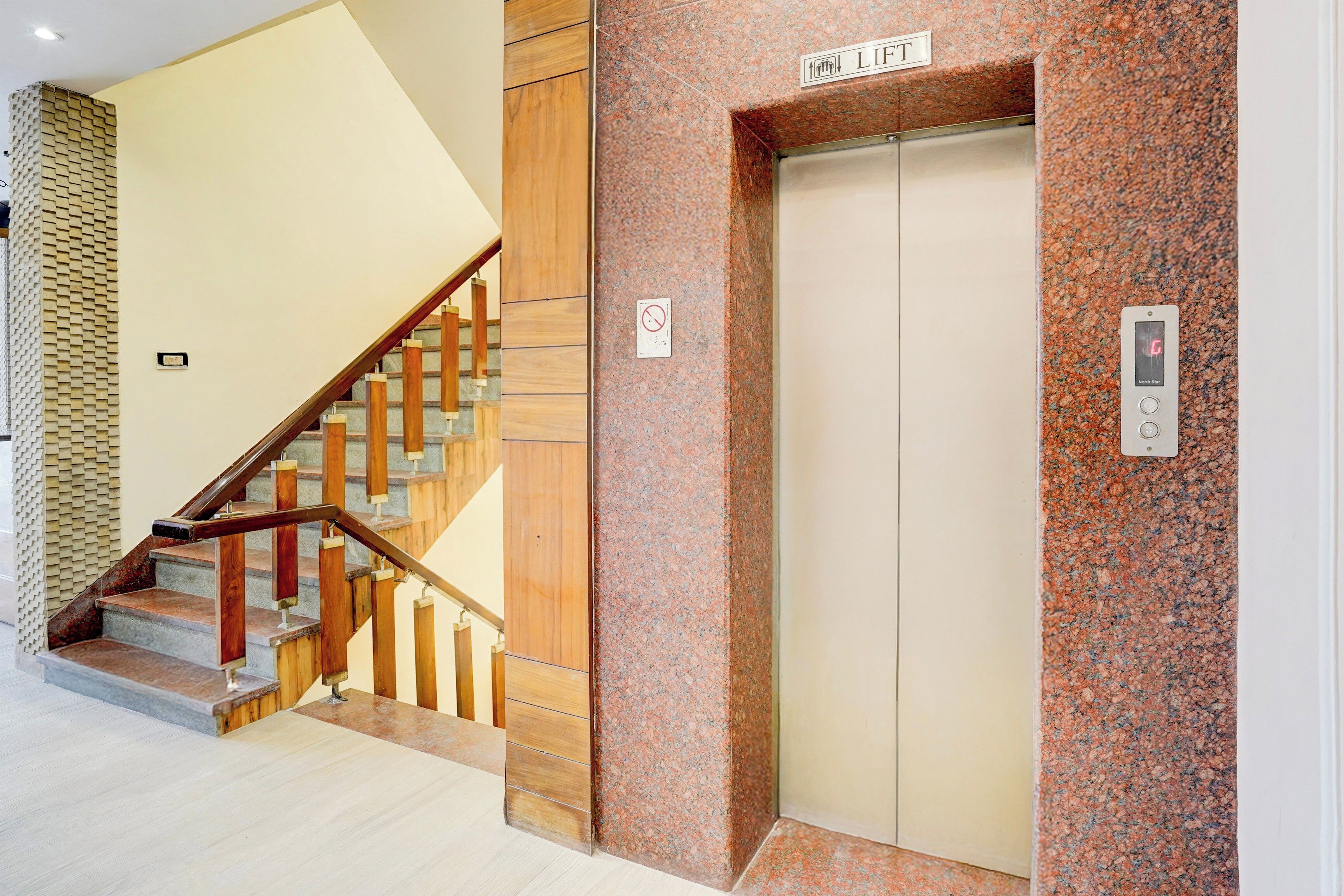 A modern elevator with a control panel, a wooden staircase with metal railings, and a textured wall.